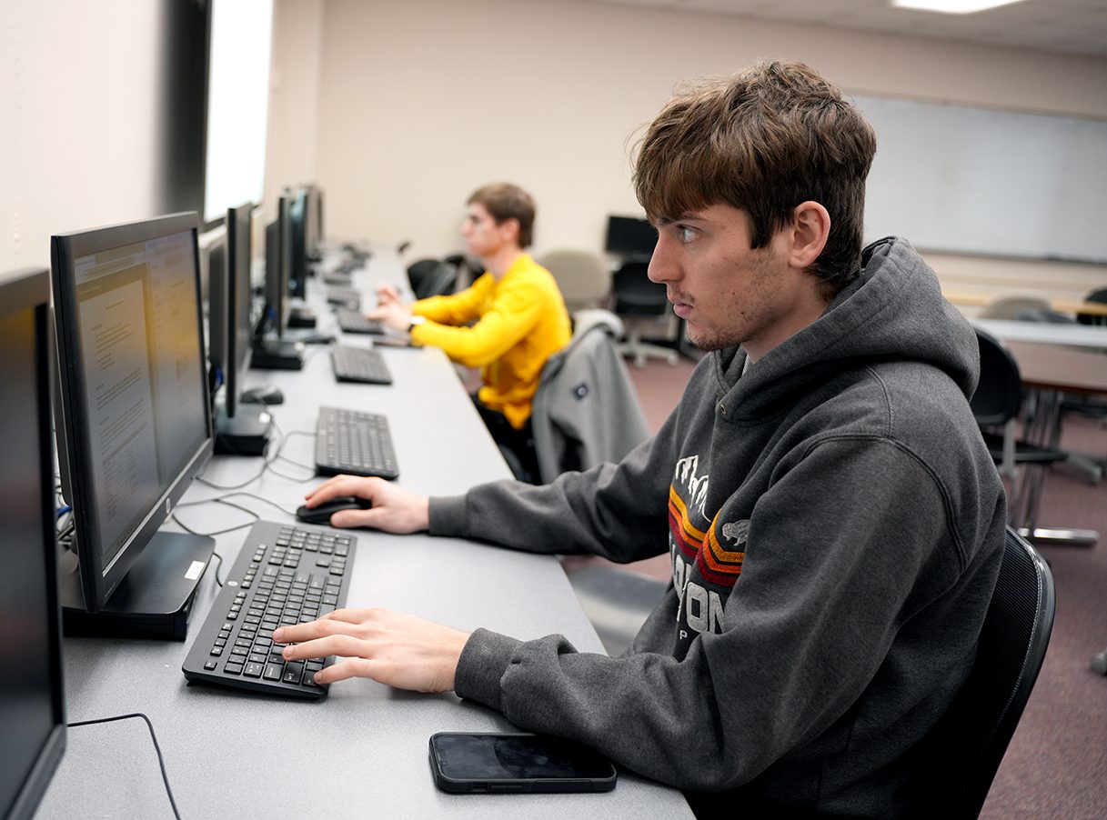 2 male students seated in front of desktop computers in computer lab