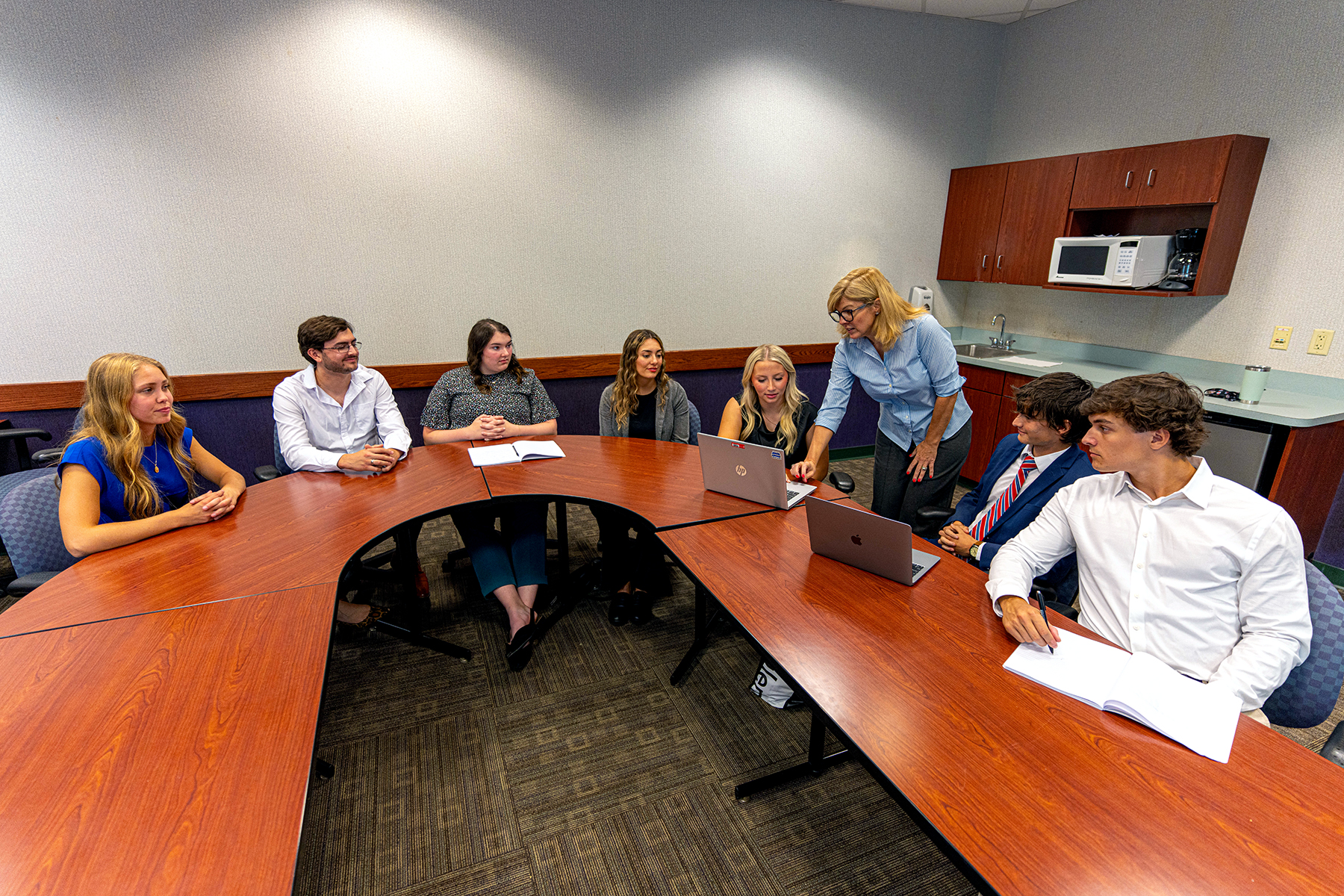 7 students and 1 female instructor positioned around curved tables in Mitchell Hall 201