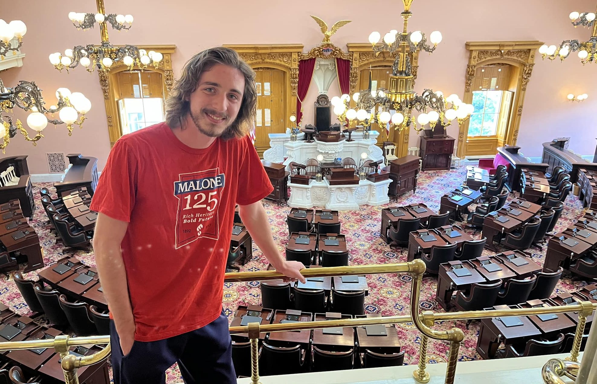male student in Malone T-shirt pictured from balcony of a room in the statehouse