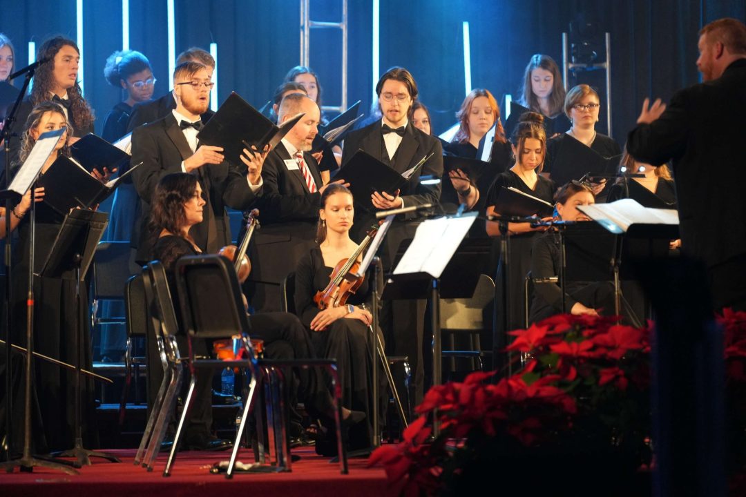 Russ Gartner conducting Chorale and alums at Christmas at Malone; strings players seated in front of Chorale