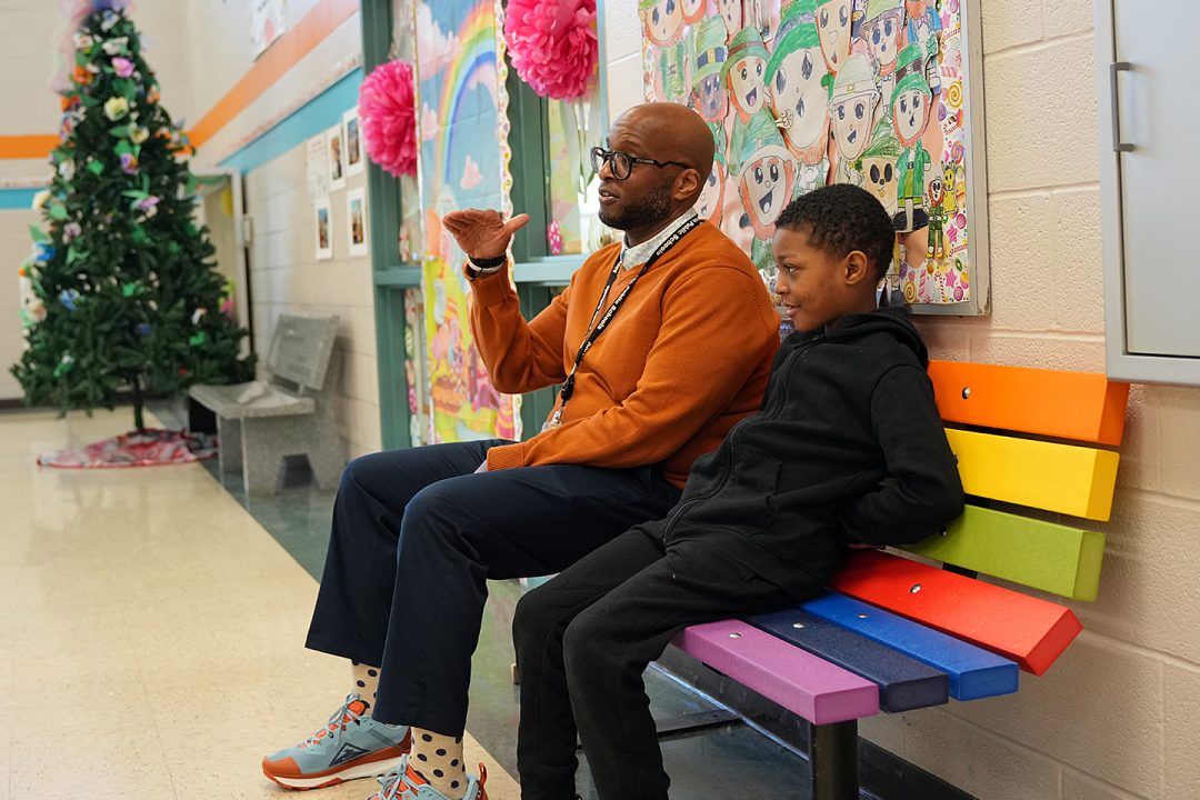 adult male counselor and young male child seated together on colorful bench