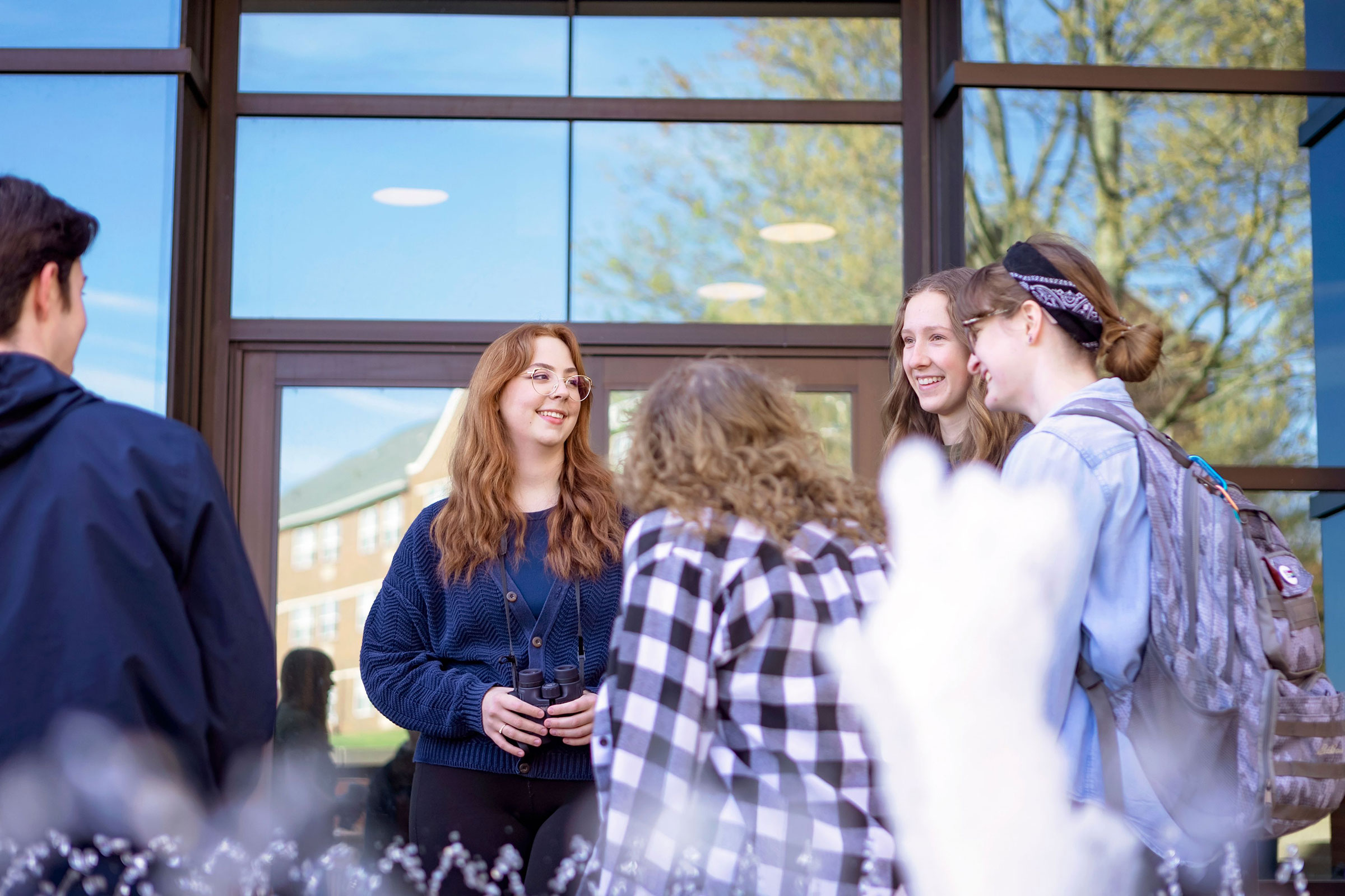 Small group of five students laugh and talk outside on the Malone campus