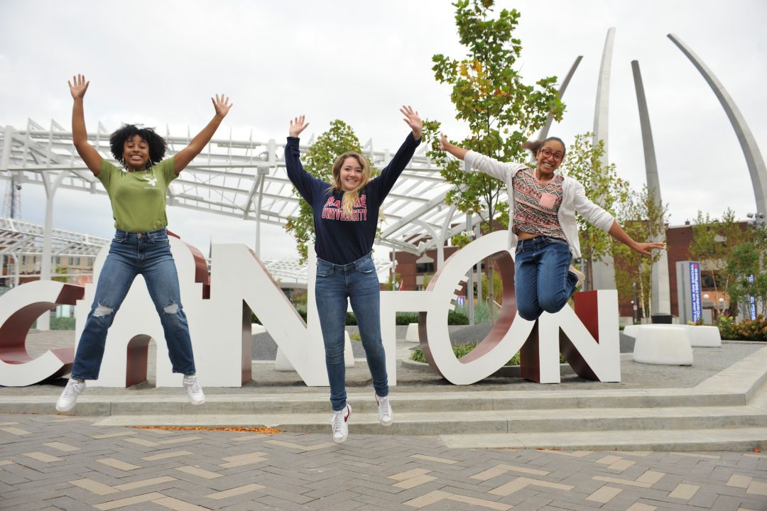 Three female students jump in front of the Canton sign in downtown Canton, Ohio