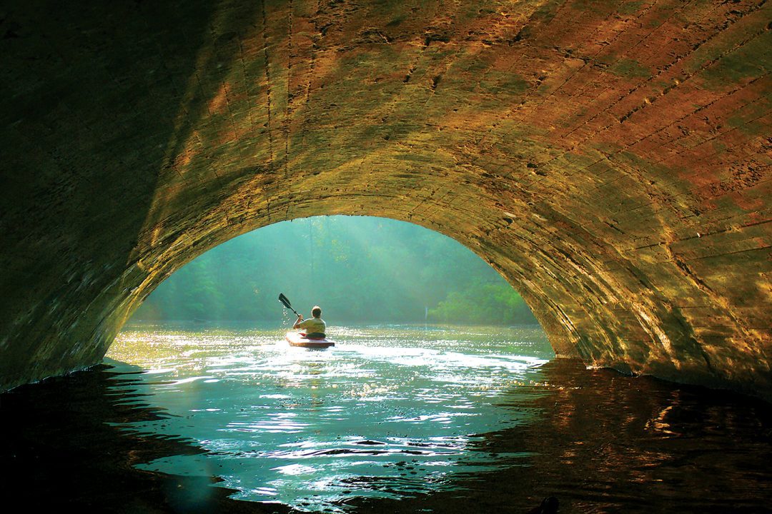 A person paddles a single kayak under a bridge in a Stark County Park